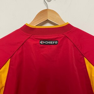 Puede incluir: Chaqueta deportiva roja y amarilla con la palabra "CHIEFS" en la espalda. La chaqueta est&aacute; colgada de una percha de madera. El cuello es amarillo y la chaqueta es roja con paneles laterales amarillos.