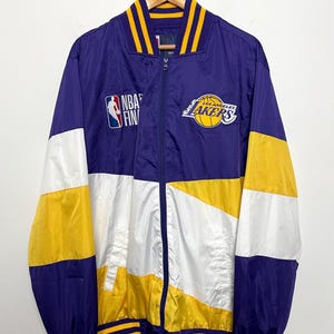 May include: A Los Angeles Lakers NBA Finals jacket in purple, white, and yellow. The jacket features the Lakers logo and NBA Finals logo on the front. The jacket has a zip-up closure and striped detailing on the collar, cuffs, and hem.