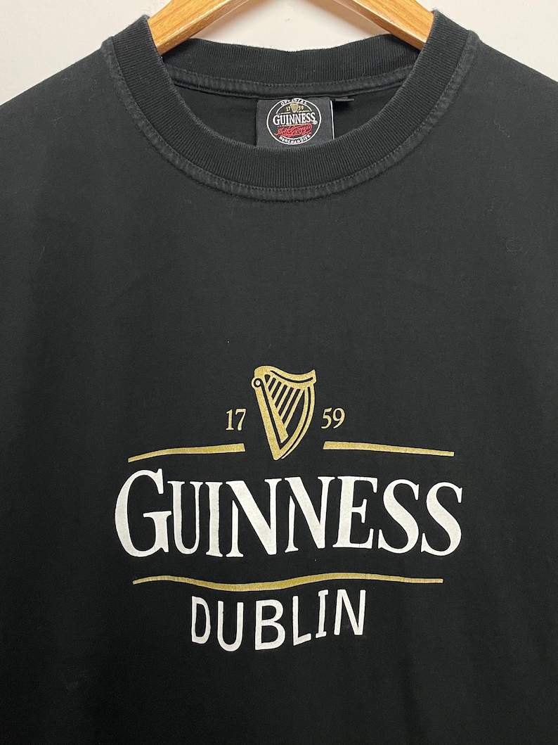 May include: Black t-shirt featuring the Guinness logo in gold and white. The logo includes a harp, the numbers 17 and 59, and the word "Dublin" beneath the Guinness name.