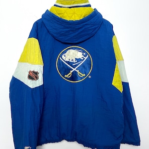 May include: Blue and yellow vintage Starter jacket featuring the Buffalo Sabres logo on the back. The jacket has a hood with a yellow lining, and yellow and white accents on the sleeves. The NHL logo is on the left sleeve.