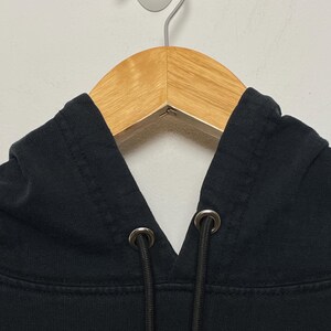 May include: Black hooded sweatshirt with a drawstring and metal eyelets. The hoodie is hanging on a wooden hanger.