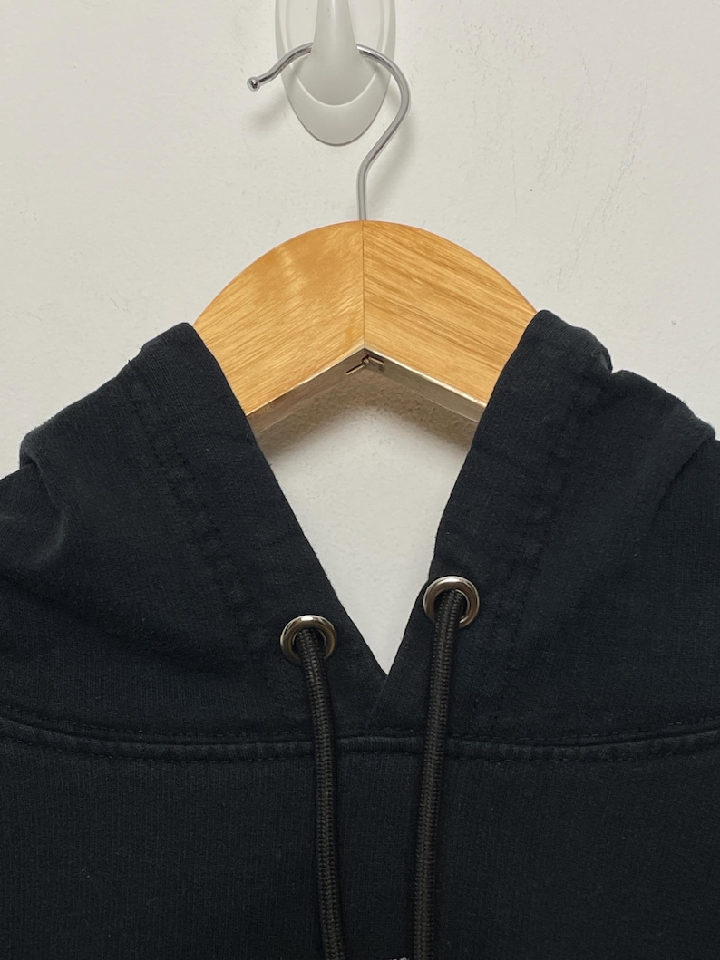 May include: Black hooded sweatshirt with a drawstring and metal eyelets. The hoodie is hanging on a wooden hanger.