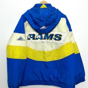 Puede incluir: Una chaqueta vintage de los Rams de color azul, amarillo y blanco con capucha. La chaqueta tiene la palabra "RAMS" en letras blancas en la parte posterior. La chaqueta tiene una cremallera y una capucha con cordón.