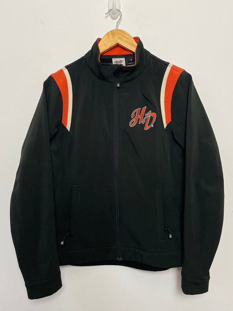 May include: Black zippered jacket with orange and white stripes on the sleeves and a Harley Davidson logo on the front.