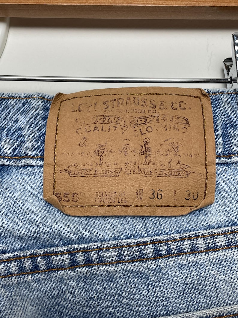 May include: Close-up of the back of blue denim jeans with a brown leather patch. The patch reads "LEVI STRAUSS & CO." and includes the text "QUALITY CLOTHING." The jeans are size W36 L30, relaxed fit, tapered leg.