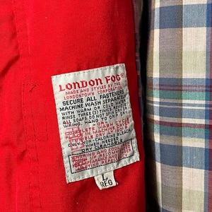 Peut inclure: Une &eacute;tiquette de veste rouge London Fog avec du texte blanc d&eacute;taillant les instructions d'entretien. L'&eacute;tiquette indique "London Fog", "Made and styled by the Londontown Corporation", "Secure all fasteners", "Machine wash separately with warm or cold water", "Rinse three (3) times. Remove all soaps. Do not spin dry or wring. Hang to drip dry.", "Complete wash cycle - or - Place in machine dryer tumble dry at 150 F", "Only non-chlorine bleach when needed", "Dry cleanable", "Washing and cool iron touch up recommended for appearance and longer lasting repellency", "L Reg".