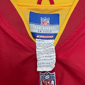 Puede incluir: Una chaqueta roja y amarilla de NFL Team Apparel con el logotipo de la NFL bordado en la parte delantera. La chaqueta tiene un cuello amarillo y un forro interior rojo. La etiqueta dice "XL Extra Large".
