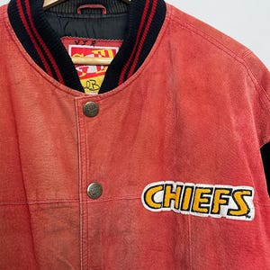 Puede incluir: Chaqueta de b&eacute;isbol de cuero rojo con ribetes negros y rojos alrededor del cuello y las mu&ntilde;ecas. La chaqueta tiene un gran parche amarillo y blanco "CHIEFS" en el lado derecho del pecho.