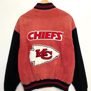 Puede incluir: Una chaqueta de b&eacute;isbol de gamuza roja y lana negra con el logotipo de los Kansas City Chiefs en la espalda. El logotipo es una punta de flecha blanca con las letras "KC" en rojo dentro. Las palabras "CHIEFS" est&aacute;n en letras blancas sobre un fondo rojo por encima de la punta de flecha.