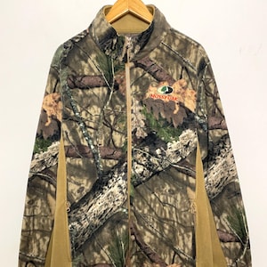 May include: A full-zip fleece jacket with a camouflage pattern in shades of brown, green, and tan. The jacket features a stand-up collar, side pockets, and the "Mossy Oak" logo. The side panels are solid tan.