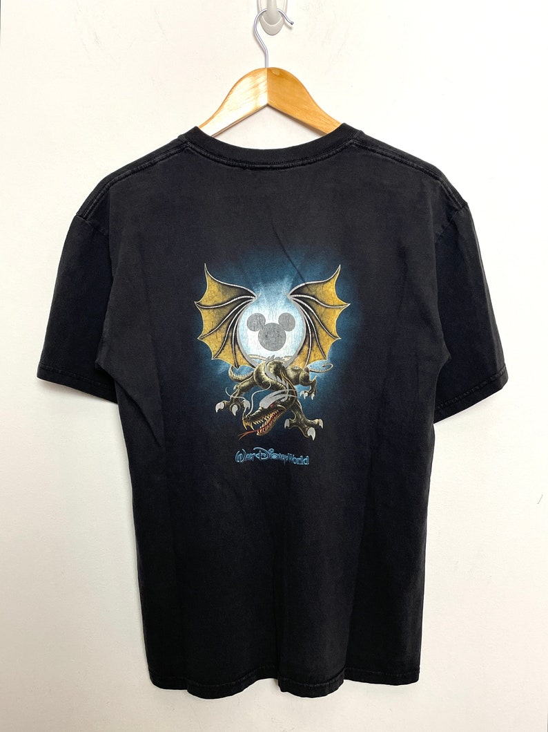 May include: Black t-shirt with a graphic of a dragon with wings and a Mickey Mouse head in a circle. The text "Walt Disney World" is printed below the graphic.