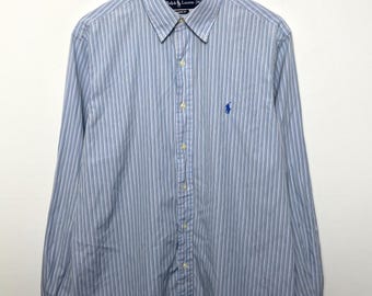 May include: A light blue and white striped button-down shirt with long sleeves, hanging on a wooden hanger. The shirt features a small blue logo on the chest and a classic collar. The shirt is made of a lightweight fabric.