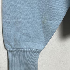 K&ouml;nnte beinhalten: Ein hellblauer Pullover mit geripptem B&uuml;ndchen. Der Pullover hat einen kleinen Fleck auf dem &Auml;rmel.