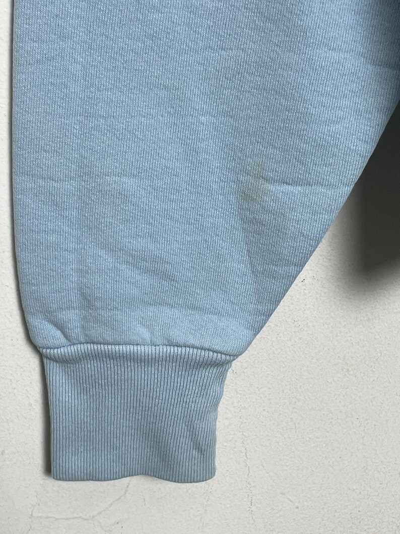 K&ouml;nnte beinhalten: Ein hellblauer Pullover mit geripptem B&uuml;ndchen. Der Pullover hat einen kleinen Fleck auf dem &Auml;rmel.