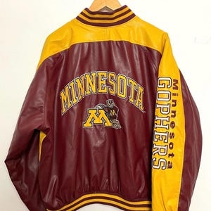 May include: Maroon and gold varsity jacket with the word "MINNESOTA" arched across the back. The jacket features the "M" logo and the words "Minnesota Gophers" down the sleeve. The jacket is hanging on a wooden hanger.