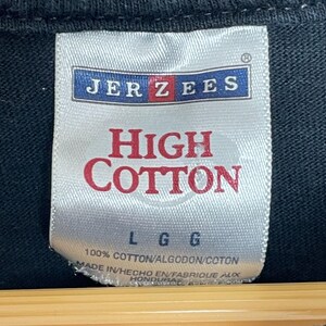 May include: Close-up of a white tag with the brand name "JERZEES" in blue and red. The tag reads "HIGH COTTON" in red, with "L G G" below. The bottom of the tag states "100% COTTON" and "MADE IN HONDURAS".