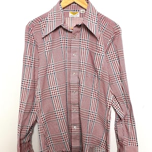 May include: A long-sleeved button-down shirt with a red, white, and blue houndstooth pattern. The shirt has a pointed collar and a single chest pocket.
