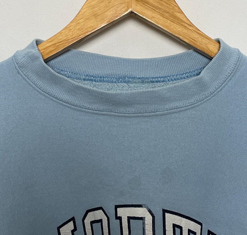 K&ouml;nnte beinhalten: Ein hellblauer Pullover mit einem wei&szlig;en und schwarzen Grafikdruck des Wortes "FORD" in gro&szlig;er, fetter Schrift.