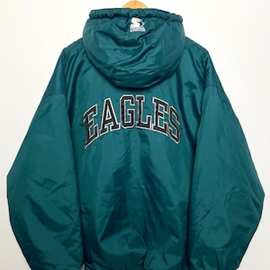 Puede incluir: Chaqueta con capucha verde azulado con la palabra "EAGLES" en letras blancas y negras en la espalda. La chaqueta tiene un logotipo de Starter en la capucha y un ribete a rayas blanco y negro en la parte inferior.