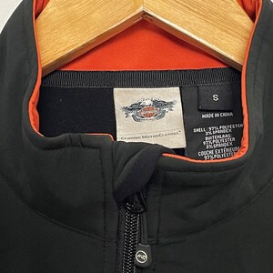 May include: Black zippered jacket with an orange lining and a Harley Davidson logo. The tag says "Genuine Motor Clothes" and lists the fabric composition as 97% polyester and 3% spandex.