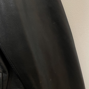 May include: Black leather jacket with a smooth texture. The jacket has a zipper closure and a stand-up collar.