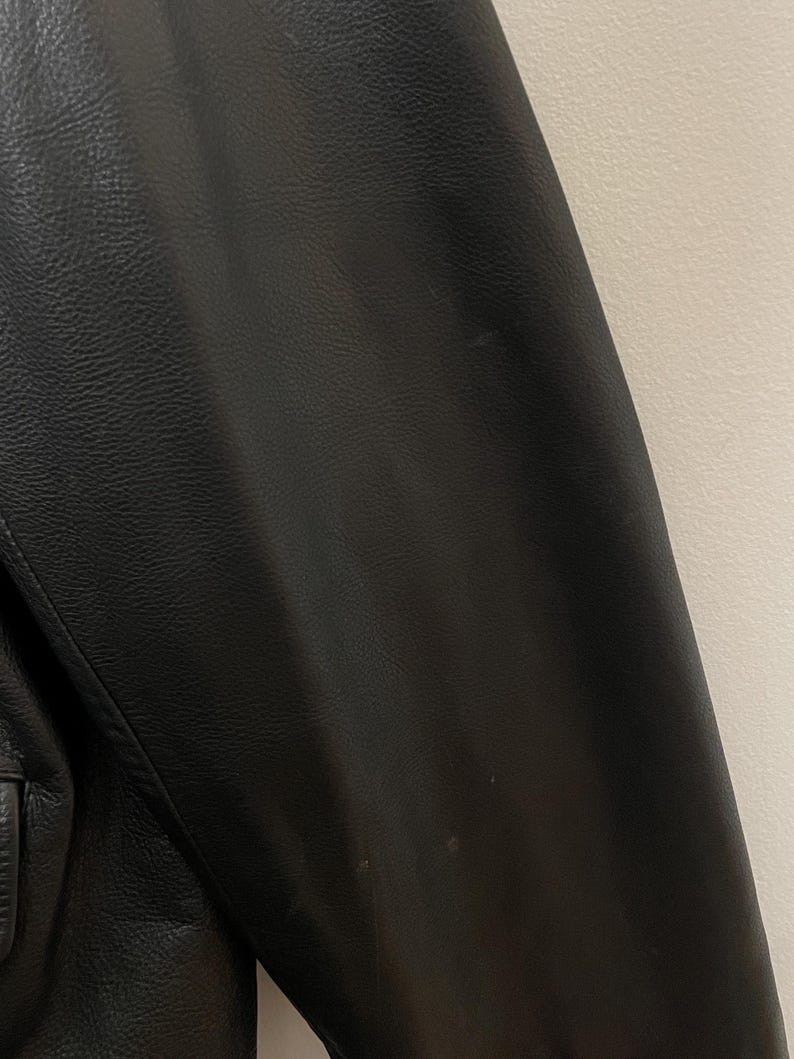 May include: Black leather jacket with a smooth texture. The jacket has a zipper closure and a stand-up collar.