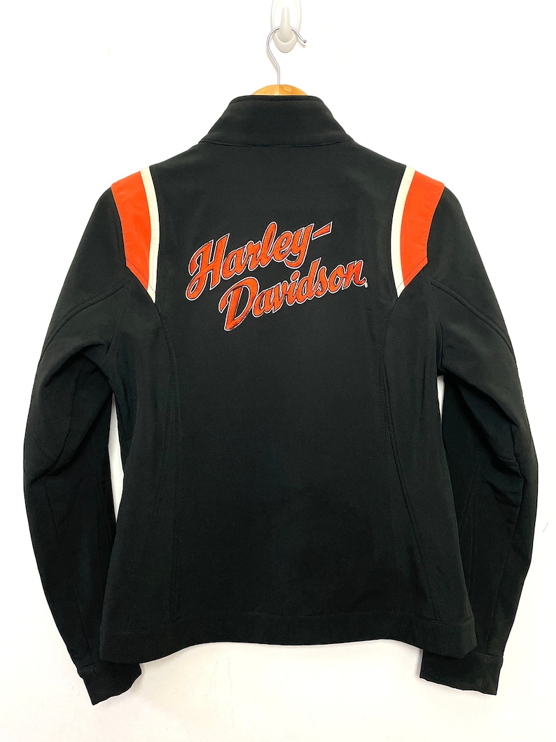 May include: Black Harley-Davidson jacket with orange and white stripes on the shoulders. The jacket has a zipper closure and a stand-up collar.