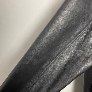 May include: Close-up of a black leather jacket sleeve. The leather has a textured, pebbled surface.