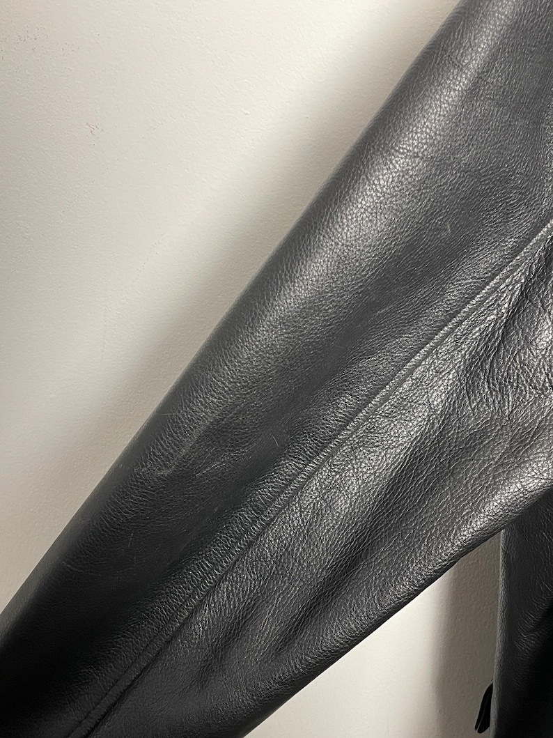 May include: Close-up of a black leather jacket sleeve. The leather has a textured, pebbled surface.