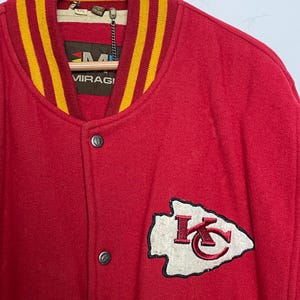 May include: Red wool varsity jacket with a yellow and gold striped collar and cuffs. Features a white and red embroidered team logo patch on the chest. The jacket has silver snap closures and a tag that reads "MIRAGI".