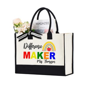 May include: A white canvas tote bag with black trim and handles. The bag has a rainbow and apple design with the text "Difference Maker" in colorful letters and "Mrs. Thompson" in black text.