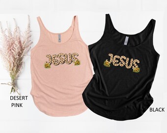 May include: Two tank tops with the word "JESUS" printed in leopard print with sunflowers on either side. The tank top on the left is a light pink color and the tank top on the right is black.