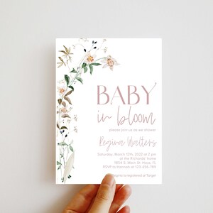 May include: A floral baby shower invitation with a watercolor design of white flowers and green leaves. The text reads "BABY in bloom" and includes the name "Regina Walters" and the date and time of the shower.