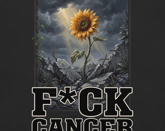 May include: A black graphic t-shirt featuring a yellow sunflower growing from gray rubble under a stormy sky with light rays. The text F*CK CANCER is printed in large, bold, white-outlined black letters at the bottom of the design.