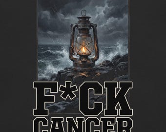 May include: A black t-shirt featuring a graphic of a lit lantern on a rocky shore during a storm, with the text F*CK CANCER printed in bold, white, block-style lettering below the image. The lantern has a cracked glass pane.