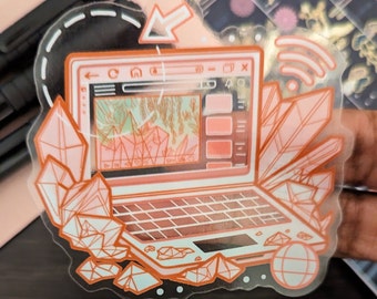 May include: A sticker featuring a pink and white laptop with a crystal design. The laptop screen shows a pink and green landscape with a crystal design. The sticker has a wifi symbol and an arrow pointing to the laptop.