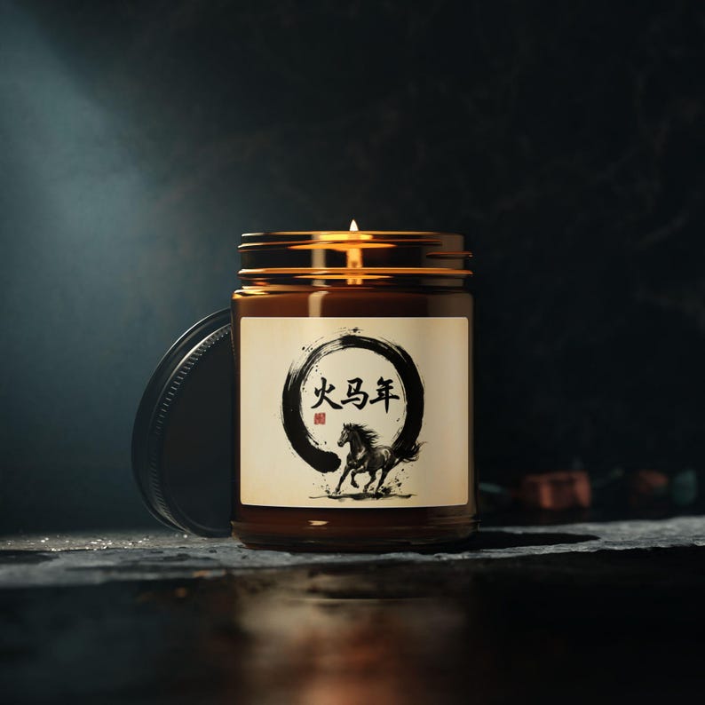 May include: A lit candle in a brown glass jar with a gold lid. The label features a black circle with Chinese characters and a black horse illustration. The jar sits on a dark surface against a dark background.