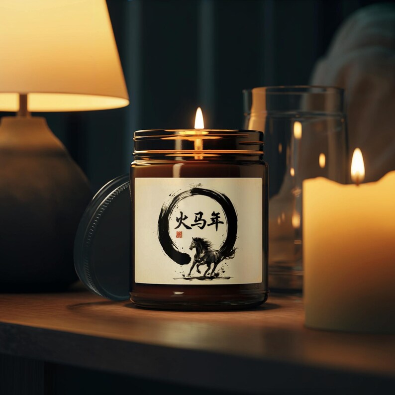 May include: A lit candle in a brown glass jar with a gold lid. The label features a black and white illustration of a horse and Chinese characters. A lit candle and a glass are in the background.