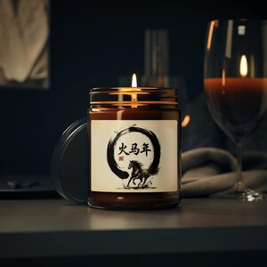 May include: A lit candle in a brown glass jar with a gold lid. The label features a black and white illustration of a horse and Chinese characters. A wine glass is in the background.