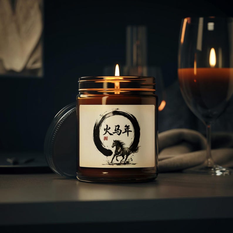 May include: A lit candle in a brown glass jar with a gold lid. The label features a black and white illustration of a horse and Chinese characters. A wine glass is in the background.