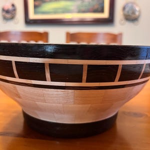 Op de afbeelding: Een houten kom met een zwart-wit geometrisch patroon. De kom is gemaakt van verschillende soorten hout, wat een uniek en prachtig ontwerp creëert.