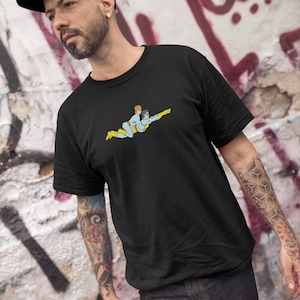 May include: Black t-shirt featuring a cartoon illustration of two figures in superhero attire flying together. The figures are in shades of blue, yellow, and tan. The shirt is being worn by a person wearing a black cap.