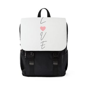 Peut inclure: Sac à dos noir avec un panneau avant blanc sur lequel est inscrit le mot "LOVE" en cursive avec un cœur rose au centre.