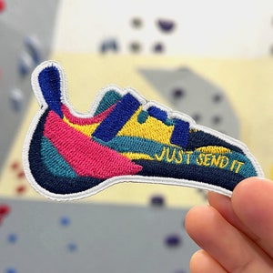 Op de afbeelding: Een kleurrijk geborduurd patch in de vorm van een klimm schoen met de tekst "JUST SEND IT" in zwart.
