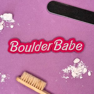 May include: Pink fabric patch with white embroidered lettering that reads "Boulder Babe".
