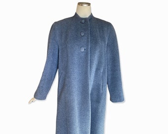 May include: A long, grey coat with a stand-up collar and three large buttons. The coat has long sleeves and two pockets. The coat is displayed on a mannequin. The coat is made of a wool-like material.
