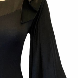 Puede incluir: Un vestido negro con un detalle de lazo &uacute;nico en el hombro. El vestido presenta una manga fluida en forma de campana. La tela parece tener textura, agregando profundidad. El vestido se exhibe en un maniqu&iacute;.