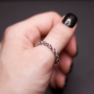 May include: A silver chain ring worn on a finger with black nail polish.