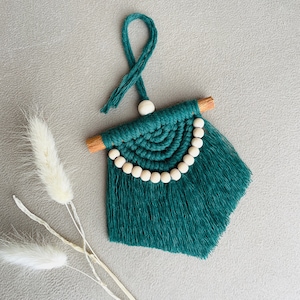 Może przedstawiać: Turkusowy makramowy wieszak ścienny z drewnianym drążkiem i frędzlami. Dekoracja ścienna ma półkolisty wzór z drewnianych koralików i pętlę do zawieszenia.