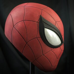 Puede incluir: Una m&aacute;scara de Spider-Man roja y negra con un patr&oacute;n de telara&ntilde;a detallado y una pieza de ojo negra con una malla blanca.